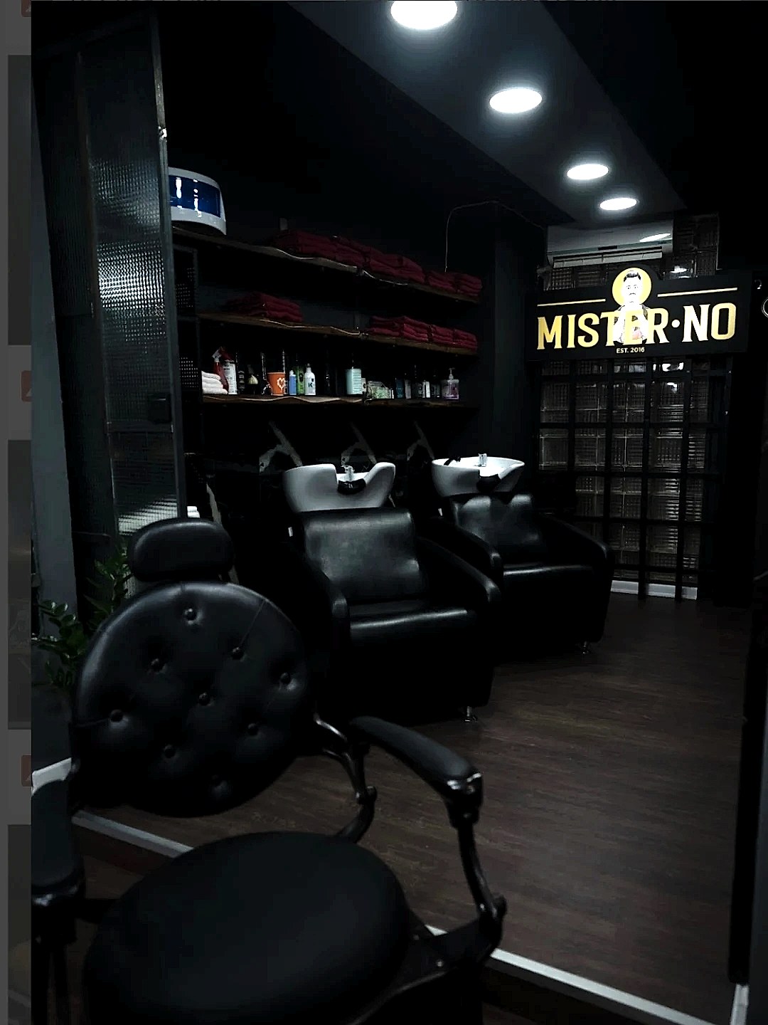 Ο χώρος του Mister No Barber Crew στην Καμάρα, με την πινακίδα MISTER NO σε χρυσό πάνω σε μαύρο, δερμάτινες καρέκλες και νιπτήρες